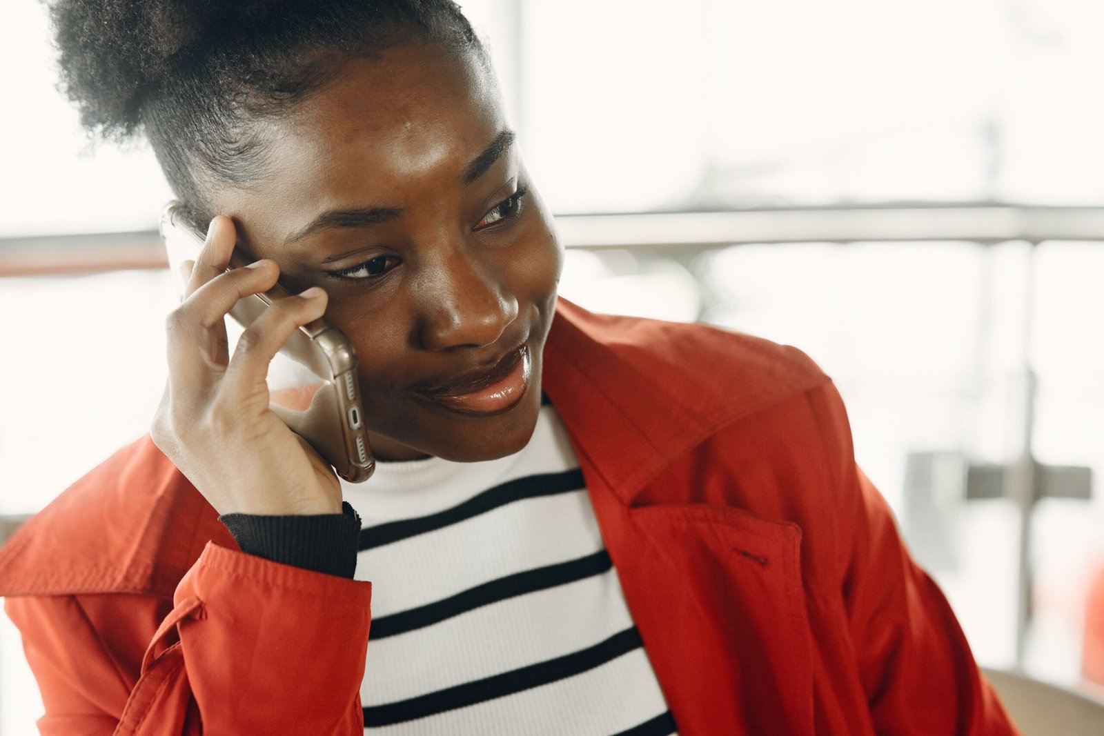 Close-up of a young woman in a red jacket talking on a cellphone indoors with a smile.